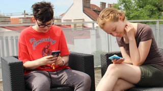Zwei Teenager sitzen und schauen auf ihre Smartphones.