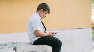 Ein Junge sitzt allein auf einer Mauer und schaut in sein Handy. 
